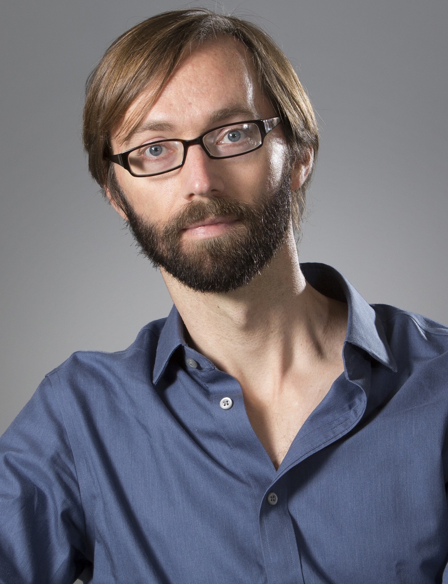 Man with brown hair and beard, glasses, and blue shirt