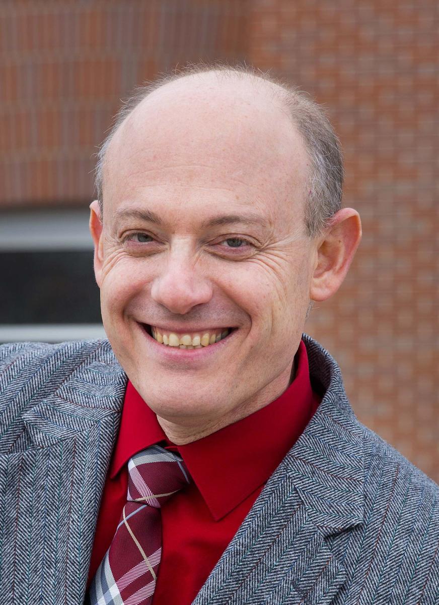 Balding man with a broad grin and scarlet button-down shirt.