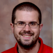 Smiling white male with dark hair and beard wearing rectangular wire-rimmed glasses and a red polo shirt.