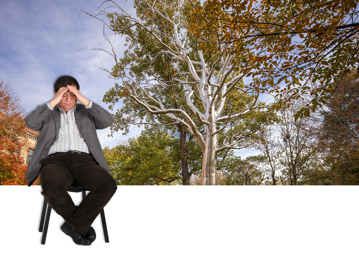 Man seated covering eyes in front of a metallic tree surrounded by greenery and a clear blue sky.